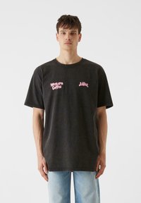 Temno siva bombažna majica s kratkimi rokavi, okroglim izrezom in sproščenim krojem. Na prsih je roza vezen napis "Western Coffee" in "Lush".