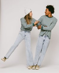 Stripete langermede skjorter i grønn og hvit, sammen med lyseblå bredbeinede jeans. Tilbehør inkluderer en hvit beanie og beige sko.