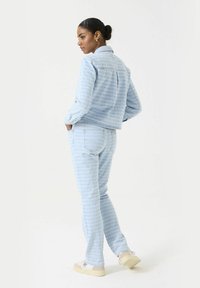 Lichtblauwe denimjas en bijpassende broek met een gestructureerd patroon. De outfit heeft een klassieke kraag en een getailleerde pasvorm.