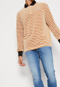 Person wearing a striped orange and white long-sleeve polo shirt with black collar and cuffs, paired with light blue jeans.