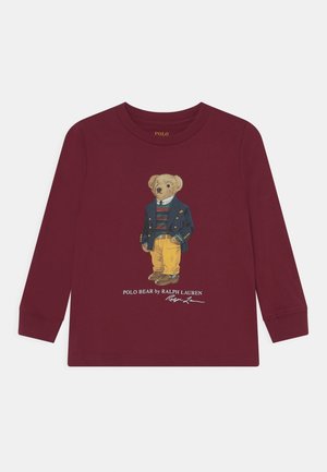 T-shirt à manches longues bordeaux avec une illustration d'un ours portant un blazer bleu, une chemise rayée et un pantalon jaune, avec un logo brodé en dessous.