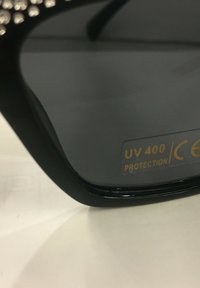 Černé sluneční brýle s texturovaným rámem, tmavými čočkami a štítkem s nápisem "UV 400 ochrana" na vnitřní straně.