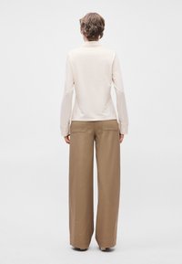 Μπεζ μπλούζα με μακρύ μανίκι και στρογγυλή λαιμόκοψη, συνδυασμένη με χαλαρές καφέ παντελόνες σε φαρδιά γραμμή που διαθέτουν δύο πίσω τσέπες. Λείος υφασμάτινος ιστός.