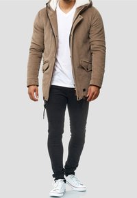 Braune Cordjacke aus Cord mit Kapuze, Fleece-Futter, Fronttaschen, kombiniert mit schwarzen Skinny-Jeans und weißen Sneakers. Schlichter Reißverschluss.