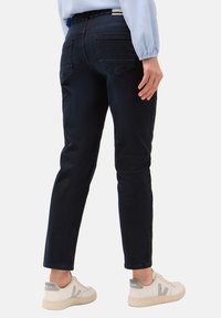 Donkerblauwe denim jeans met een slim fit, voorzien van geborduurde achterzakken en een soepele textuur, gecombineerd met witte sneakers met grijze accenten.