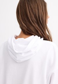 Sudadera blanca con capucha, que presenta una textura suave y un ajuste relajado. La capucha tiene un diseño de doble capa para mayor calidez.