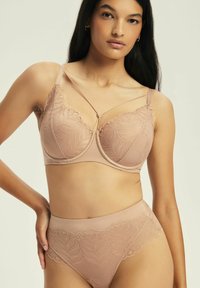 Jasnobrązowy biustonosz z koronkowym pokryciem w kwiaty, z fiszbinami i ozdobnymi ramiączkami. Wysokie majtki w tym samym stylu mają podobne detale koronkowe.