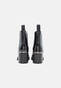 Černé lakované kožené kotníkové boty s robustním podpatkem, elastickými bočními panely a zlatým akcentem kolem spodní části. Hladká textura, elegantní design.