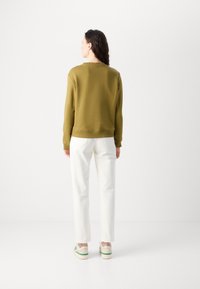 Sweatshirt vert olive, manches longues, poignets et ourlet côtelés ; associé à un pantalon droit blanc et des chaussures décontractées avec des accents verts.