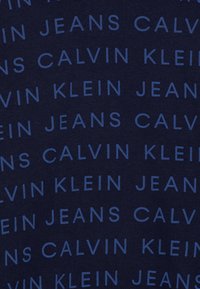Tessuto brandizzato Calvin Klein in blu navy con motivo di testo ripetuto che presenta "CALVIN," "JEANS" e "KLEIN" in un blu più chiaro.