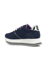 Sneaker in suede blu navy con suola intermedia bianca, suola grigia, dettaglio metallico sul tallone e occhielli viola. Presenta una punta arrotondata e una collana imbottita.