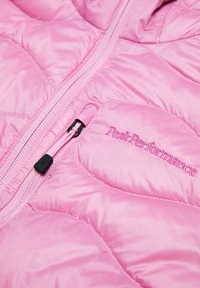 Veste matelassée rose avec coutures diagonales, une fermeture éclair à l'avant et "Peak Performance" brodé sur la poche poitrine.