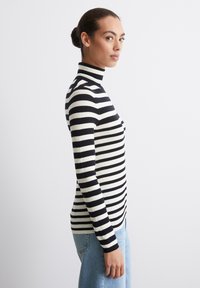 Zwart-wit gestreepte coltrui, aansluitend ontwerp, geribbelde textuur, contrasterende kleuren, gestyled met lichtblauwe jeans.