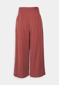 Wide-leg trousers in rust-colored fabric, featuring a high waist, pleats, and a smooth texture. Clean lines and no visible hardware.