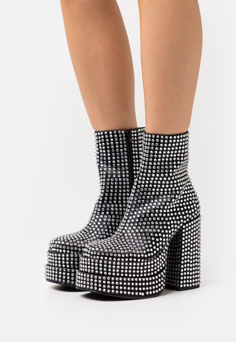 Bottines à plateforme noires ornées de clous argentés, dotées d'une fermeture éclair latérale et de talons épais, avec une texture lisse et une finition brillante.