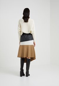 Maglione bianco lavorato a maglia con trama aperta, gonna in pelle a blocchi di colore nera e marrone, e stivali neri al ginocchio con tacco a blocchi.