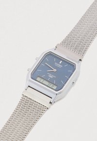 Orologio al quarzo con cinturino a maglia d'argento, quadrante blu navy, cassa argento e display digitale. Caratteristiche includono resistenza all'acqua e lancette luminescenti.