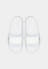 Λευκές σανδάλες με φάσα, με υφή και γεωμετρικά σχέδια στην πάνω πλευρά, δύο λευκές λωρίδες και χρυσό λογότυπο στο πλάι.