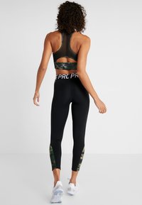 Leggings deportivos negros con acentos de camuflaje, que cuentan con una cinturilla alta y un sujetador deportivo de espalda nadadora con un panel de malla y una banda inferior de camuflaje.