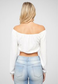 Bílý crop top s odhalenými rameny a dlouhými rukávy, texturovaná tkanina, spárovaný s vysokými modrými džíny s zadními kapsami.