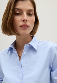Light blue button-up shirt with a classic collar and a smooth texture; features white buttons and a clean, tailored fit.