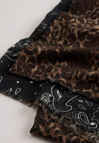 Leopardprint en paisley-gebloemde sjaals in zwart en bruin; zachte stof met franjeranden, gelaagd voor extra textuur.