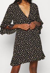 Schwarzes Kleid mit tiefem V-Ausschnitt, kurzen, ausgestellten Ärmeln und einem Muster aus kleinen gelben und rosa Blumen. Weicher Stoff mit fließender Silhouette.