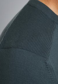 Dunkelgrüner Strickpullover mit einem gerippten Muster an den Schultern, glatt gewebtem Stoff am Körper und kontrastierenden Nähten.