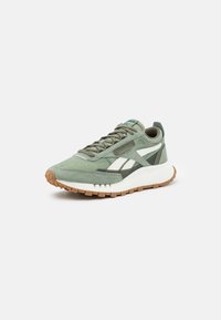 Green suede athletic shoe with white accents, fabric laces, and a textured rubber sole. Features a retro design and cushioned collar.