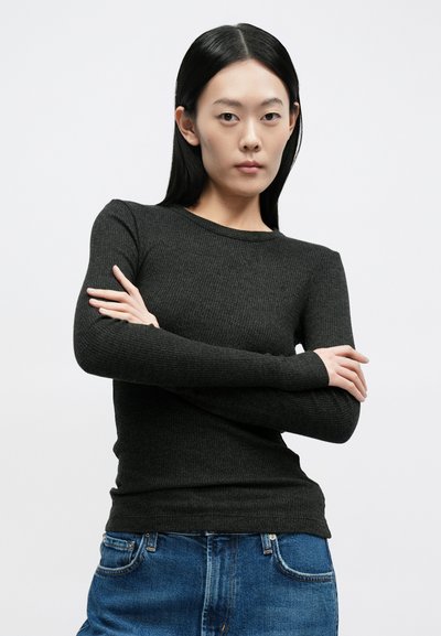 Μπλούζα μακρυμάνικη σε σκούρο γκρι με ριμπ ύφανση και στρογγυλή λαιμόκοψη. Διαθέτει εφαρμοστή γραμμή και επιμηκυμένες μανσέτες. Συνδυάζεται με μπλε τζιν παντελόνι.