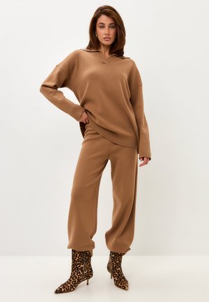 Brown knit sweater with a v-neck and dropped shoulders paired with matching loose-fitting pants and leopard print ankle boots.