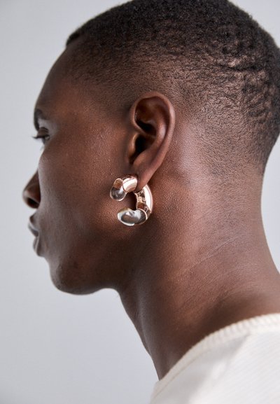 Gold and silver hoop earrings with smooth, rounded shapes, featuring transparent accents. Worn on a dark-skinned male model's ear.