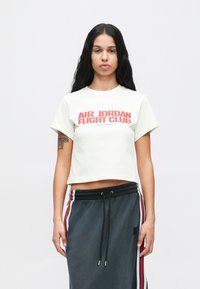 Λευκό κοντομάνικο μπλουζάκι με κόκκινη γραφιστική "AIR JORDAN FIGHT CLUB", σε συνδυασμό με σκούρες γκρι φόρμες που διαθέτουν πλαϊνές λωρίδες.