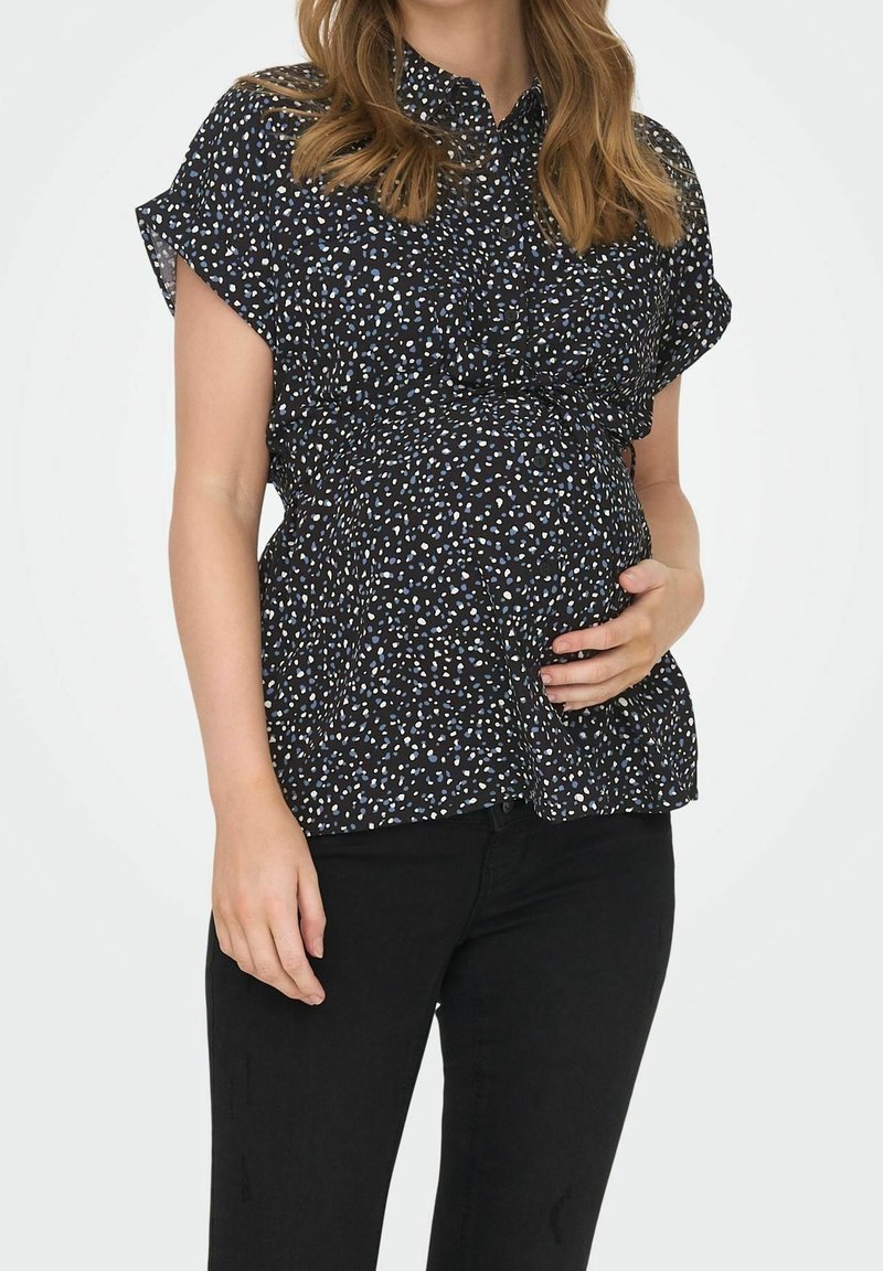 Blouse de maternité en tissu noir avec un motif dispersé de petites taches bleu clair et blanches, manches courtes, coupe décontractée et col.