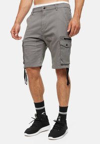 Shorts cargo gris avec poches latérales, détail de fermeture éclair et sangles ajustables aux jambes. Fabriqués en tissu durable, dotés d'une coupe classique et d'une taille.