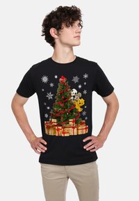 Svart t-shirt med en färgglad julgran-design med dekorationer, omgiven av mjuka leksaker och guldinslagna paket med röda snören.