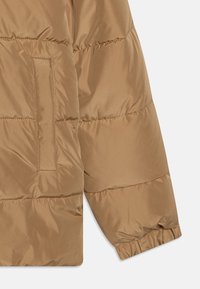 Brun puffjacka med ett kviltat mönster, slät struktur, elastiska muddar och en sidoficka för praktisk användning.