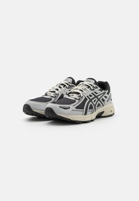 Sport shoes in gray and black, featuring a mesh upper, rubber outsole, and contrasting white laces. Notable logo on the tongue.