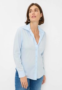 Light blue button-up shirt with long sleeves, a collar, and a front placket. Made of a smooth fabric, featuring a relaxed fit and cuffed sleeves.