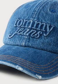 Džinsinė kepurė su siuvinėtu mėlynu "tommy jeans" logotipu, kontrastingomis rudos spalvos siūlėmis palei kraštelį ir tekstūruota audinio medžiaga.