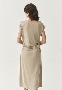Abito beige al ginocchio con maniche corte, caratterizzato da arricciature sul retro. Tessuto morbido e liscio con un design a vestibilità rilassata.