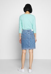 Džínová sukně s vlnitým lemem a vyšitým květinovým vzorem, zkombinovaná s mintově zeleným topem s dlouhým rukávem a bílými teniskami.