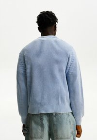 Ljusblå stickad tröja med lång ärm och rund halsringning. Har ett strukturerat vävt mönster och en åtsittande passform i midjan.