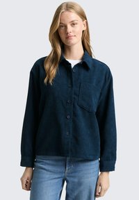 Marineblauwe corduroy overhemd met een knoopsluiting aan de voorkant, borstzak en lange mouwen met een getextureerd, ribbelpatroon.