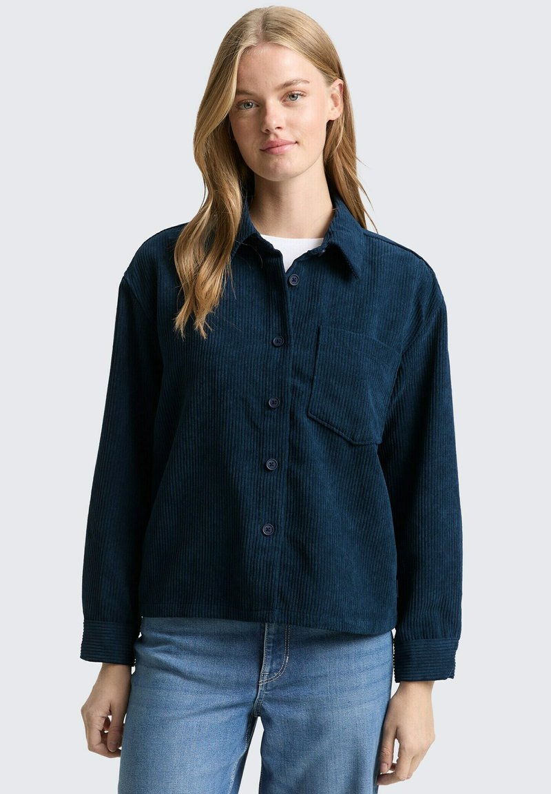 Marineblauwe corduroy overhemd met een knoopsluiting aan de voorkant, borstzak en lange mouwen met een getextureerd, ribbelpatroon.