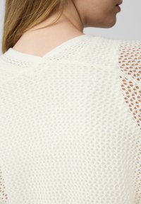 Witte gebreide sweater met een gemêleerd patroon, een V-vormige halslijn en open-stikselaccenten op de schouders.