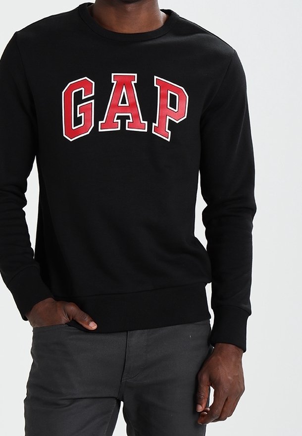 Sudadera negra con el logo rojo de "GAP" en un diseño arqueado. Presenta un cuello redondo y puños de punto. Tejido suave con una textura lisa.