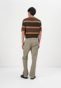 Gebreid shirt met korte mouwen in bruin en oranje horizontale strepen, gecombineerd met beige cargobroek en zwarte sandalen.