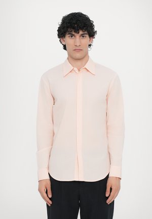 Camisa de botones de manga larga color durazno en tejido ligero. Cuenta con un cuello clásico, plisado frontal y dobladillo redondeado con puños abotonados.