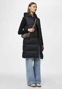 Gilet imbottito nero con cappuccio, chiusura a zip e cuciture orizzontali. Abbinato a jeans svasati blu chiaro e una borsa a tracolla con stampa leopardata.